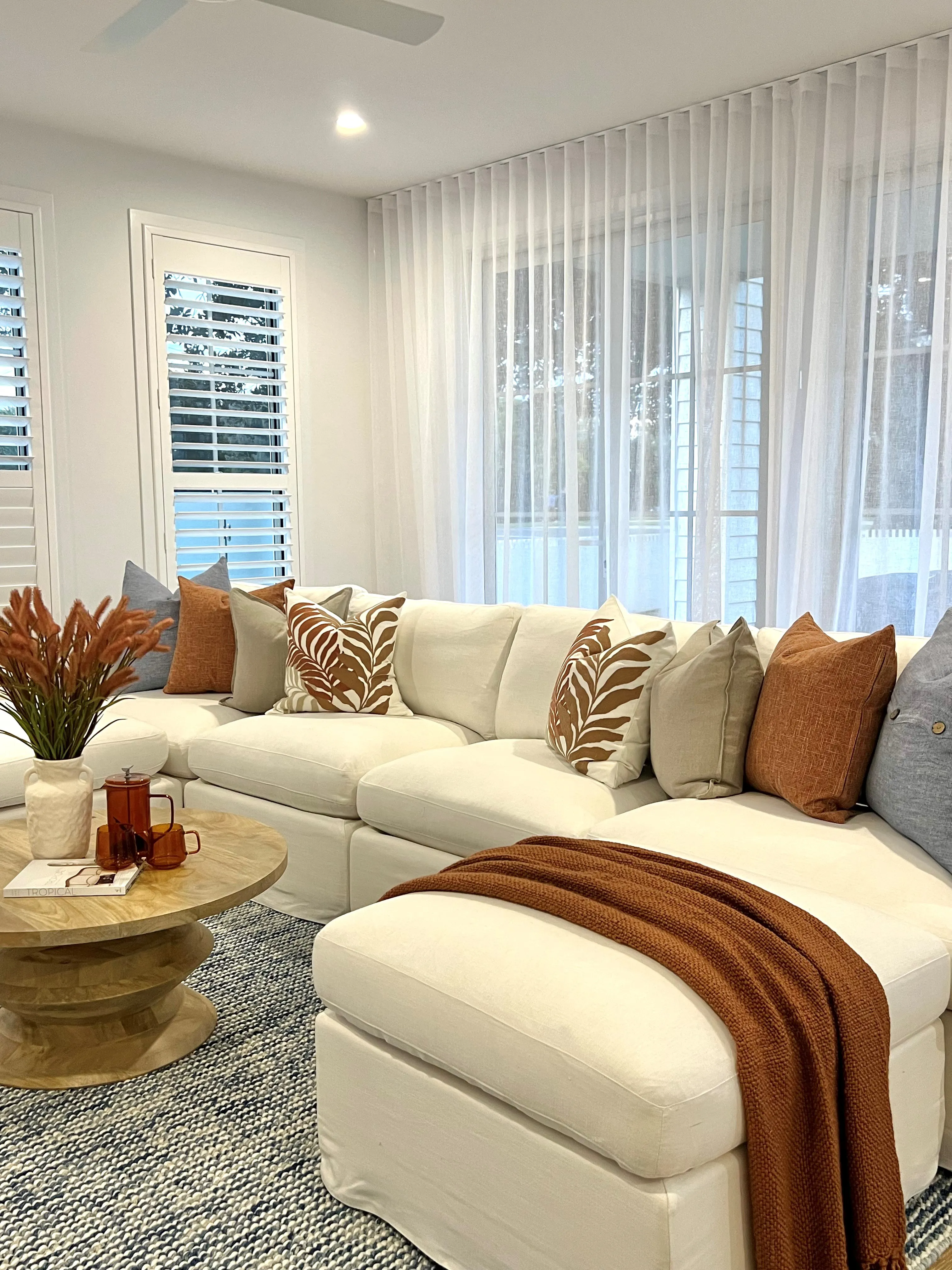 Family room detail with cream modular sofa, terracotta and palm cushions and sheer curtains
